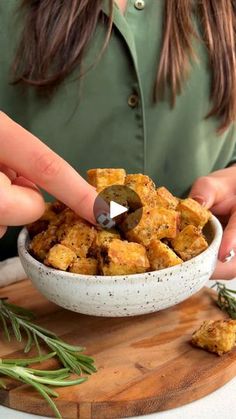 a woman is dipping something into a bowl with rosemary sprigs on the side