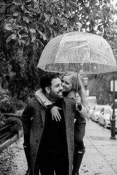 black and white photograph of a man carrying a woman under an umbrella in the rain