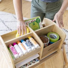 a woman standing in front of a wooden box filled with craft supplies