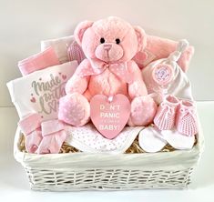 a pink teddy bear sitting on top of a white basket filled with baby clothes and accessories