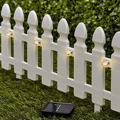 a white picket fence with lights on it and a cell phone in the grass next to it