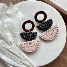 two pairs of black and pink earrings on a white plate with feathers in the background