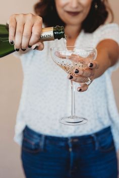 a woman pouring champagne into a wine glass with her hands and nails on the rim