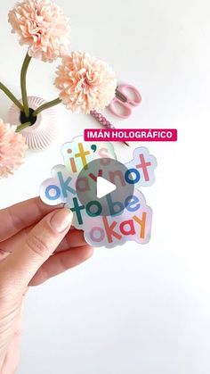 a person holding up a sticker with the words okay to be okay on it