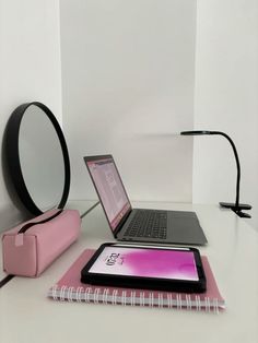 an open laptop computer sitting on top of a white desk next to a pink notebook