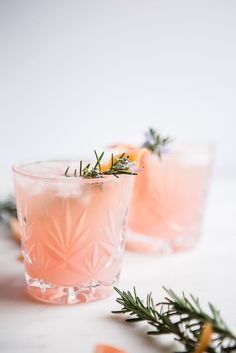 two glasses filled with pink lemonade and rosemary garnish on a white surface