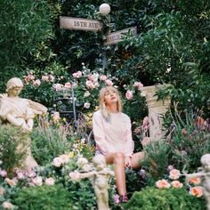 a woman sitting on the ground in front of some flowers and statues with a street sign above her head