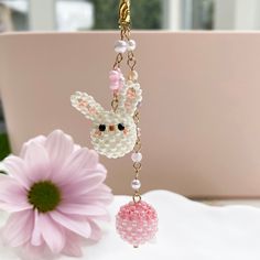 a beaded keychain hanging from a chain next to a pink flower on a table