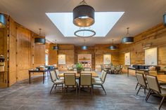 a large dining room with wooden walls and ceiling lights is pictured in this image, there are many chairs around the table