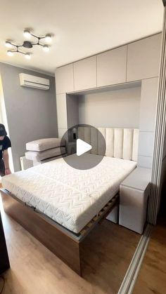 a person standing next to a bed in a room with white walls and wooden floors