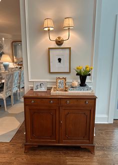 a wooden cabinet with two pictures on top and flowers in vases next to it