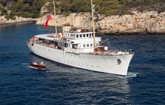 a large white boat in the middle of the ocean near some rocks and water with a red flag on it's mast