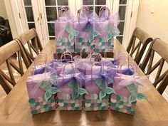 there are many bags on the table with purple and green bows around them, all wrapped in cellophane