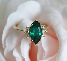 an emerald and diamond ring sitting on top of a white rose