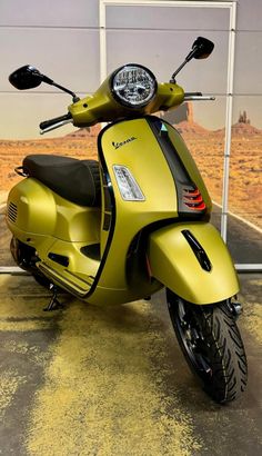 a yellow scooter parked in front of a wall with a painting on it