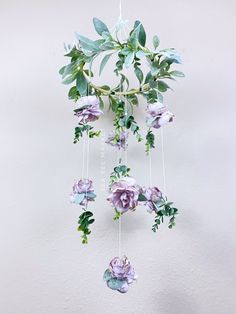 a mobile with flowers and leaves hanging from it's sides on a white wall