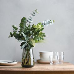 a vase filled with flowers on top of a wooden table next to plates and cups