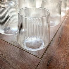 three clear glass cups sitting on top of a wooden table next to another glass cup