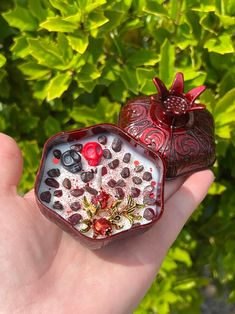 a hand holding two small red and white vases in front of some green plants