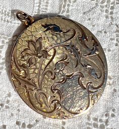 "Dating from the Art Nouveau period, early 1910s, this unique locket has a gorgeous botanical theme.  The flower blossom and flower buds are on curvy stems, accompanied by engraved leaves, all on a fancy, engine-turned background.  There is a blank shield at the bottom for monograming, but it was never used.  The back is shiny with a mirror finish.  The inside is signed \"1874\" over \"R.B.M.\" over \"ATRICE.\" The locket is by the R. B. MacDonald & Company, which was founded in 1874 in Attlebor Victorian Flower-shaped Collectible Jewelry, Victorian Flower Jewelry Collectible, Victorian Flower Collectible Jewelry, Victorian Flower Jewelry For Collectors, Vintage Medallion Jewelry With Flower Charm, Antique Engraved Flower Jewelry, Antique Flower Engraved Jewelry, Vintage Engraved Flower Pendant Jewelry, Unique Locket