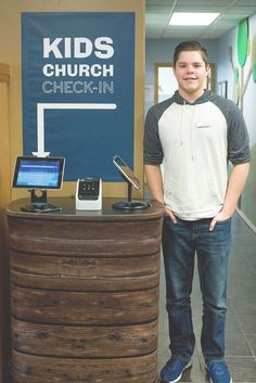 a young man standing in front of a desk with a laptop on top of it