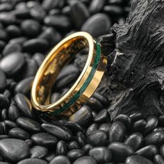 a gold and green wedding ring sitting on top of black rocks next to a tree