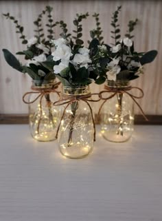 three mason jar vases with flowers and string lights on the lids are sitting on a table