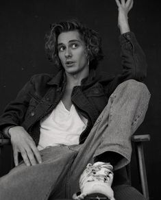 a black and white photo of a man sitting in a chair with his hand up