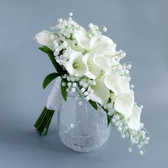 a bouquet of white flowers in a glass vase on a gray background with greenery