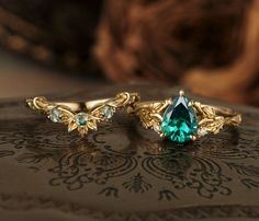 two gold rings with green and white stones on top of a lace covered table cloth