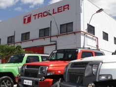 several trucks are parked in front of a large white building with a red and green truck on it's side