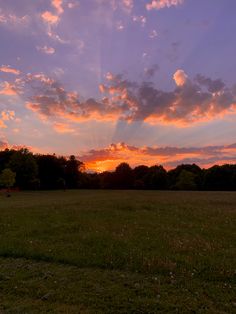 the sun is setting over an open field with trees in the background