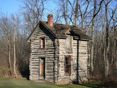 an old log cabin sits in the middle of a wooded area with no leaves on it