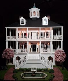 a doll house with white balconies and pink flowers in the front yard at night