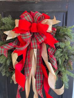 a christmas wreath with red and gold ribbons hanging on a front door, decorated with pine cones