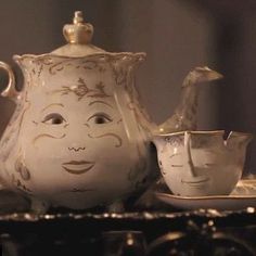 a white tea pot sitting on top of a table next to cups and saucers