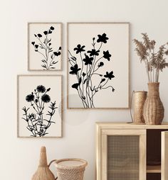 three black and white flowers are displayed on the wall above a wicker basket with vases