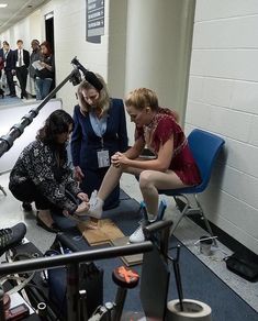 three women sitting on chairs in a room with microphones and other people standing around