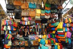 a woman sitting in front of a display of handbags and purses at a market