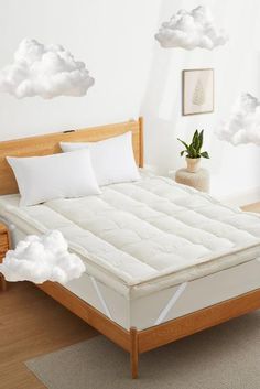 a bed with white sheets and pillows in a room next to a wall with clouds painted on it