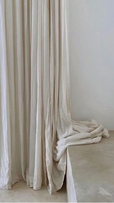 a white curtain is open in the corner of a room with concrete floor and walls