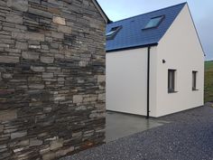 a white house with a blue roof next to a stone wall