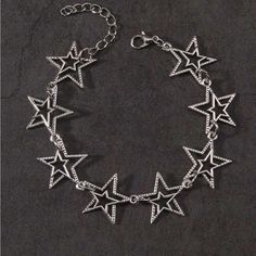 a silver bracelet with stars on it and a chain hanging from the middle, sitting on a black surface