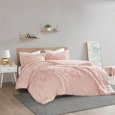 a bed with pink comforter and pillows in a room next to a white table