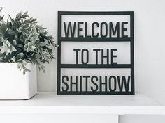 a sign that says welcome to the shitshow next to a potted plant