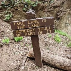 a wooden sign sitting on the side of a dirt road next to a tree trunk