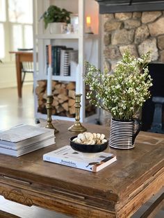 a wooden table topped with books and a vase filled with flowers next to a fire place