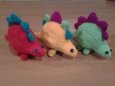 three knitted toy animals sitting next to each other on a wooden table with one stuffed animal in the middle