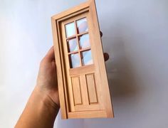 a hand holding a small wooden door in it's right hand and the bottom half is open