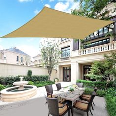 an outdoor dining area with table and chairs under a large beige shade over the water fountain